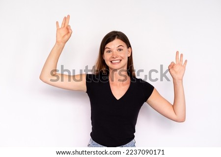 Portrait of excited young woman making ok gesture over white background. Caucasian lady wearing black T-shirt and jeans looking at camera and smiling. Success and happiness concept
