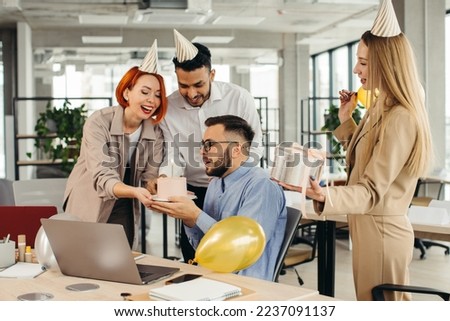 Happy businessman blowing out a candle on cake while celebrating Birthday with female coworkers in the office.