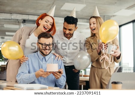 Young man is going to blow candles on cake and make a wish while celebrating birthday with colleagues. Colleagues celebrating a birthday in the office