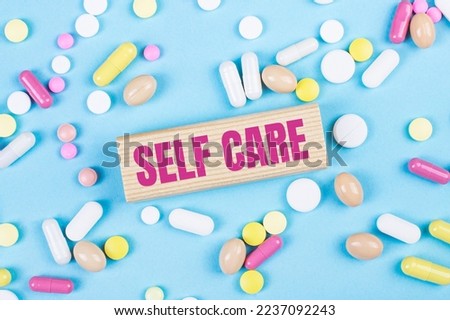 On a blue background, multi-colored pills and a wooden block with the text SELF CARE. View from above. Medical concept