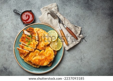 Crispy panko breaded fried chicken fillet with green salad and lemon cut on plate on gray background table with ketchup from above. Japanese style deep fried coated chicken breasts, space for text. Royalty-Free Stock Photo #2237093185