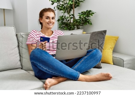 Young woman using laptop and credit card sitting on sofa at home