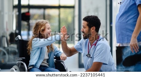 Young multiracial doctor having fun with little girl on wheelchair.