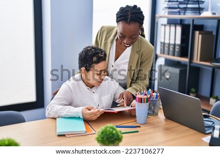 African american mother and son using laptop and reading book at office