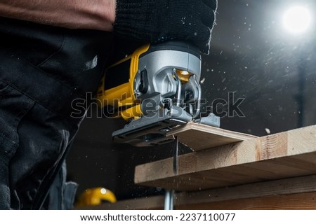 Close-up of a man cutting a wooden plank with an electric jigsaw in a workshop. Royalty-Free Stock Photo #2237110077