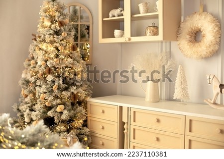 Interior kitchen in winter decor. Vase with snow branches and toy rocking horse on table. Stylish cozy scandi cuisine interior decor with decorated Christmas tree. Ceramic utensil and decor on shelfs.