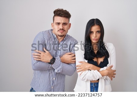 Young hispanic couple standing over white background shaking and freezing for winter cold with sad and shock expression on face 