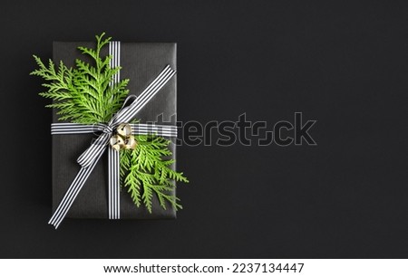 Black gift box with sprig of thuja and bells on black background. Space for your text.