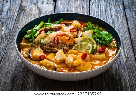 Tom Yum - Thai soup with halibut nuggets and rice noodles on wooden table 