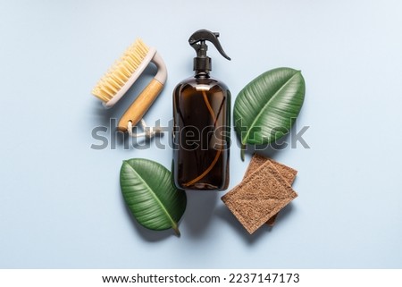 Glass refillable cleaning spray bottle on blue background with bamboo eco sponges and green leaf.  Zero waste cleaning concept background with copy space