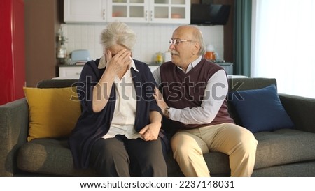 An elderly couple sitting in their armchair at home. Image of an elderly couple in troubled marriages. Old man comforting his crying, sad wife.