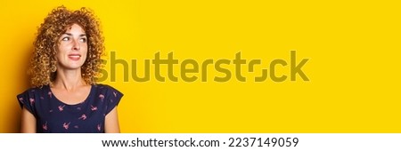 affable curly young woman looks to the side on a yellow background. Banner