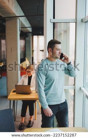 Business man, manager looking out of window in deep thought, standing at workplace with phone in office, thinking about future of company, thinking about solution for work task