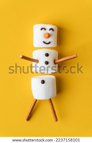 Happy funny marshmallow snowman on the yellow background. Flat lay. Copy space for a free text. Anticipation of Christmas. Winter concept background.