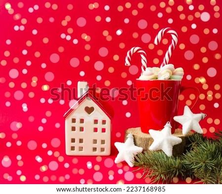 New Year decorative card.  On a red background, a New Year's house in shiny lights next to a red cup with sweets marshmallow marshmallows and cane canes.  Front view, Christmas and New Year concept.
