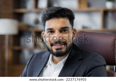 Close up portrait of bearded handsome successful middle east smiling businessman sitting at chair, working in his modern office.