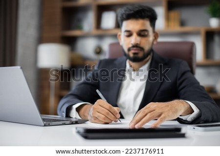 Focus on hands, young bearded male accountant working from modern office using laptop while holding a document and pen in his hands and sign new deal or writing report.