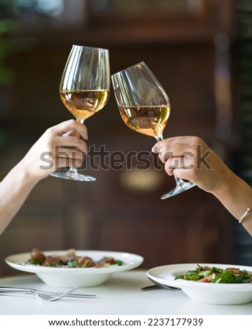 Two women are drinking wine. Two glasses of white wine in female hands. Lunch at restaurant. Wine and vegetable salad. Italian food. Italian restaurant. Soft focus. Royalty-Free Stock Photo #2237177939