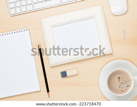 Photo frame on office table with notepad, computer and coffee cup. View from above