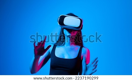 Portrait of brunette woman in a black top with 3D virtual reality glasses enjoys his trip in an adventurous world in neon light. Concept of connection technology with science, augmented reality.