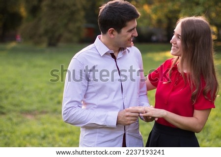 Man in love proposing to his girlfriend outdoors in the park, putting the engagement ring on her finger.