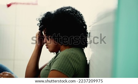 One desperate young black woman suffering from mental problems on kitchen floor. Dramatic African American adult person suffers from depression illness Royalty-Free Stock Photo #2237209975