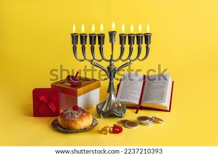 Image of Jewish holiday Hanukkah with menorah (traditional Candelabra), donuts and wooden dreidels (spinning top), doughnut, chocolate coins on a yellow background.