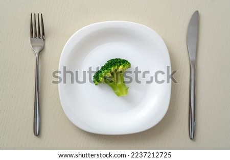 A small portion of boiled broccoli on a white plate with a knife and fork, minimum calories Royalty-Free Stock Photo #2237212725