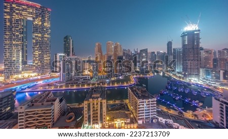 Dubai Marina panorama with boats and yachts parked in harbor and illuminated skyscrapers around canal aerial night to day transition timelapse before sunrise. Towers of JBR district on a background