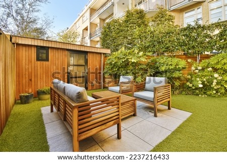 a backyard area with wooden furniture and green grass on the ground in front of an apartment building that is surrounded by trees