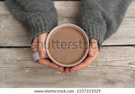 Female hands in a grey sweater holding a mug of hot chocolate on a rustic wooden background with a copy space