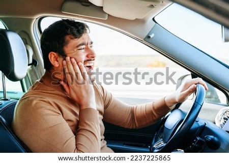 Side view young male driver holding on to the tooth while sitting in the car. Neuralgia and toothache greatly upset a guy with a beard in a brown sweater. Dental diseases and sensations. Royalty-Free Stock Photo #2237225865