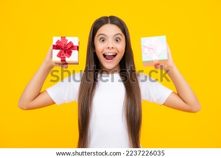 Teenager child holding gift box on yellow isolated background. Gift for kids birthday. Christmas or New Year present box. Excited teenager, glad amazed and overjoyed emotions.