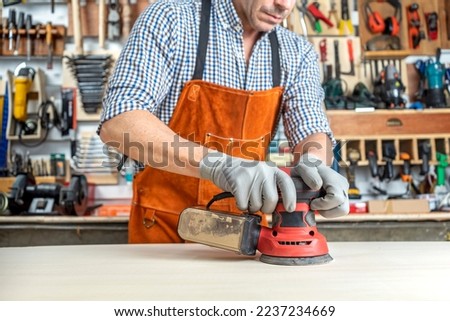 CARPENTER IN WORKSHOP WORKING WOOD WITH AN ORBITAL SANDER. SMALL BUSINESSES AND SELF EMPLOYED. DIY CONCEPT. Royalty-Free Stock Photo #2237234669