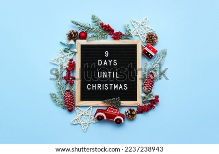 Black felt letterboard with countdown surrounded by winter decoration on blue background. 9 days until Christmas. Twenty-four day series of postcards. Selective focus