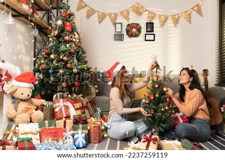 Asian women friends sit on the floor and decorating small christmas tree together with wrapped gift box around her in warm living room for christmas event Royalty-Free Stock Photo #2237259119