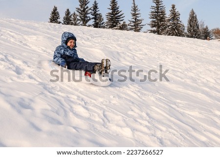 Young boy sliding down a snowy hill in a toboggan