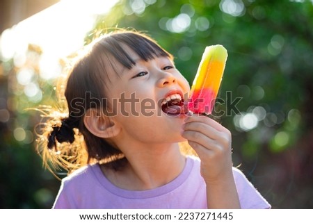 Cute happy baby girl eating ice cream popsicle in summer. Picture for concept of sweet, fat, obesity and diabetes in children. Soft focus.