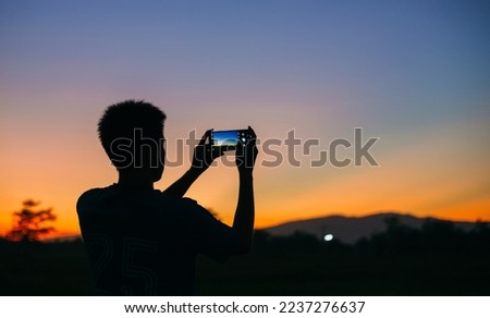 Silhouette man takes photo of the mountain landscape with his smart phone, a view from the back. travel in summer, outdoor activities