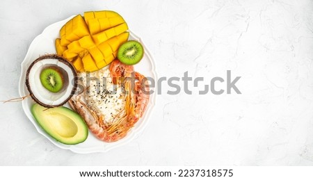 Poke bowl with avocado, shrimp, rice, mango, kiwi and coconut on a light background, healthy and balanced food. Long banner format. top view.