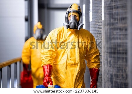 Portrait of industrial worker in hazmat protection suit and gas mask working inside chemicals production plant. In background large tanks with acid and factory interior. Royalty-Free Stock Photo #2237336145