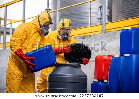 Workers wearing protection suit and gas mask mixing dangerous chemicals inside production plant. Royalty-Free Stock Photo #2237336147