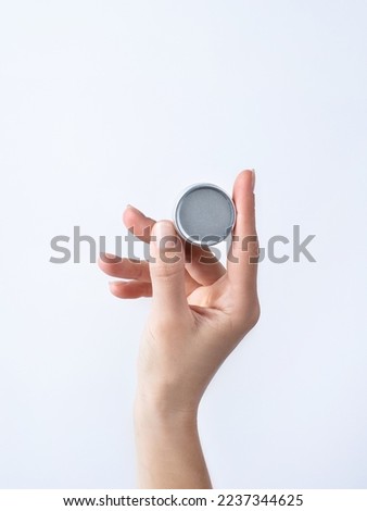 Woman hand holding blank round tin container for lip balm or cream on light gray background. Cosmetic beauty product branding mockup. Copy space