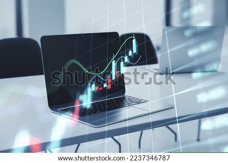 Close up of laptop on desktop with glowing business forex chart hologram and grid on blurry background. Trade, stock, finance and invest concept. Double exposure Royalty-Free Stock Photo #2237346787