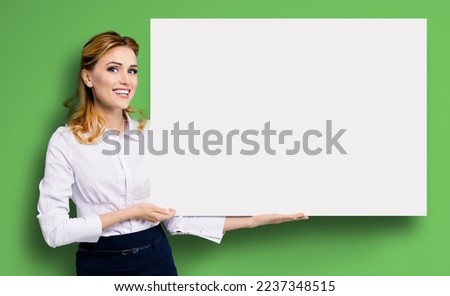 Happy excited smiling business woman in white confident clothing showing blank banner signboard. Success and advertising concept. Copy space empty place for some text. Bright green background.