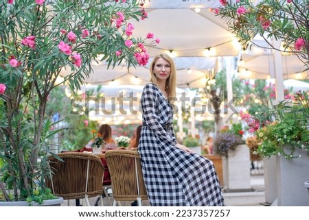 Banner with an attractive blonde Caucasian man sitting in a summer cafe where blooming rose bushes and bokeh lights in the background. Urban lifestyle concept