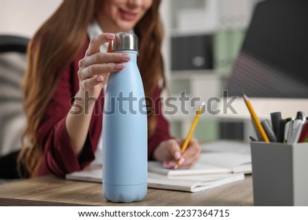 Woman holding thermos bottle at workplace, closeup Royalty-Free Stock Photo #2237364715