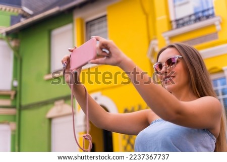 Portrait attractive young blonde woman taking a photo, behind yellow and blue colorful facade