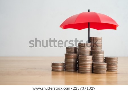 Stacked coins is protected by red umbrella on wooden table white wall background copy space. Assets wealth, money saving or money investment protection, security by insurance concept. Risk management. Royalty-Free Stock Photo #2237371329
