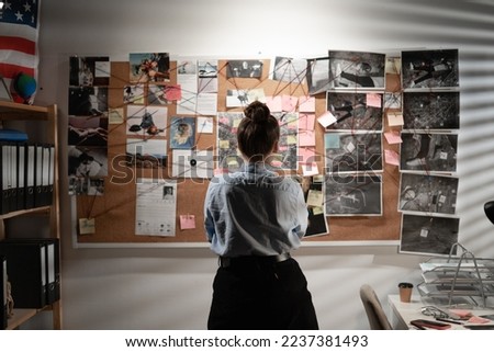 Young female detective looking at evidence board, back view. Copy space Royalty-Free Stock Photo #2237381493
